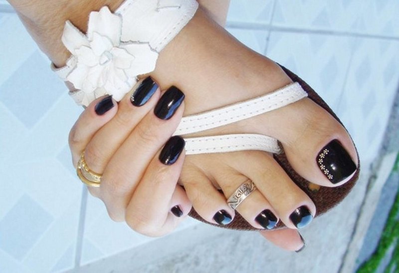 Fashionable black pedicure Black gel polish with flower pebbles